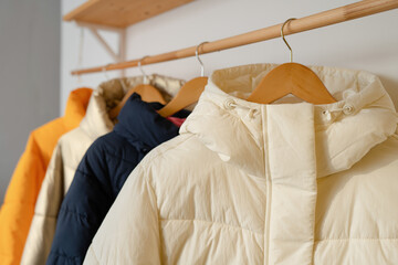 Winter clothes on a hanger in the room. A row of down jackets hang on a white background.