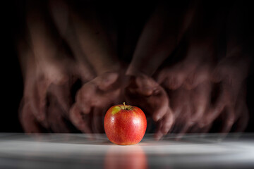 Chciwe ręce pożądają jabłka leżącego na stole. Kuszenie - obrazy, fototapety, plakaty