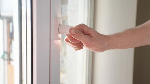 Close-up hands of unrecognizable man closing pvc window by handle after ventilate room at sunny day. Concept of ventilating housing, fighting mold, fresh air, saving heat. Shooting in slow motion.