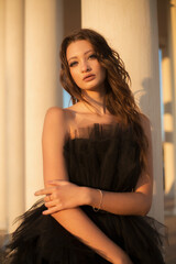 sexy attractive young girl model brunette with long hair in a black long and short mesh dress in black high-heeled shoes with beautiful long legs with makeup and hairstyle against a blue sky portrait 