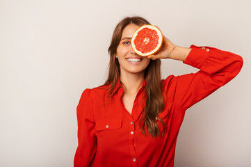 Young smiling blonde woman wearing red shirt covers one eye with half a grapefruit.