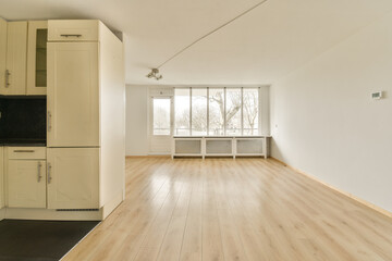 an empty room with wood floors and white cabinets on either side, there is a large window to the left