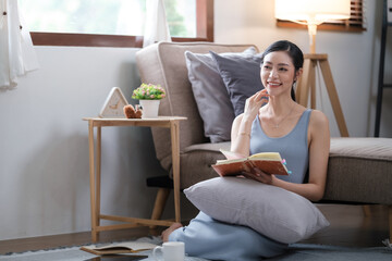 Happy young woman reading book on sofa at home. Lifestyle freelance relax and chill drinking coffee in living room. Lifestyle Concept