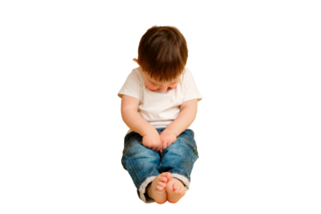 Full length portrait of an embarrassed toddler baby on a studio isolated on a white background. Shy child sitting on the floor in a white t-shirt and blue jeans. Kid aged one year and four months