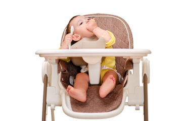 Happy toddler baby boy learns to eat porridge himself with a spoon while sitting in a child chair, isolated on a white background. Smiling child eats with his hands and a spoon, kid aged one year