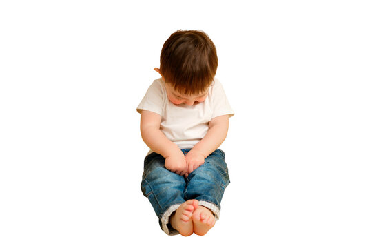 Full length portrait of an embarrassed toddler baby on a studio isolated on a white background. Shy child sitting on the floor in a white t-shirt and blue jeans. Kid aged one year and four months