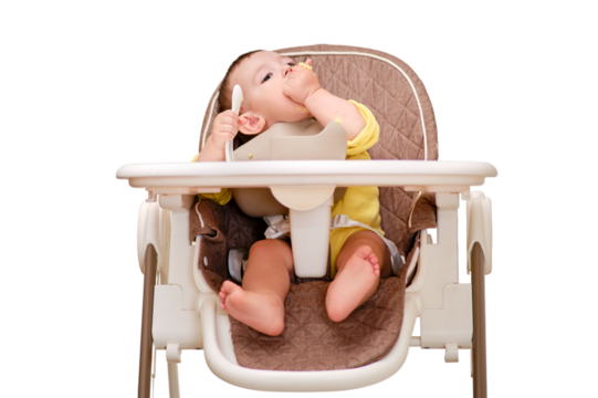 Happy toddler baby boy learns to eat porridge himself with a spoon while sitting in a child chair, isolated on a white background. Smiling child eats with his hands and a spoon, kid aged one year