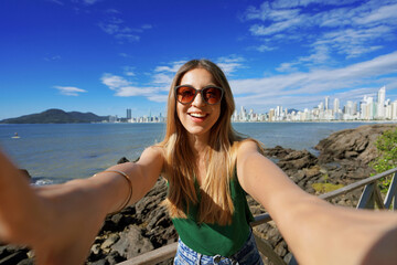 Naklejka premium Trendy millennial girl having fun takes self portrait on summer vacation in Balneario Camboriu, Brazil