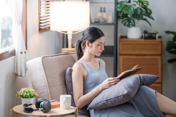 Happy young woman reading book on sofa at home. Lifestyle freelance relax and chill drinking coffee in living room. Lifestyle Concept