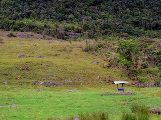 A blue trough for cattle, with a tin roof, stands in a grassland near a native forest in the central Andean mountains of COlombia near the town of La Palma.