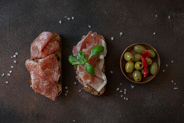 Set of appetizers - crackers with cheese, salami, prosciutto, tomato, olives and salad on dark brown background 