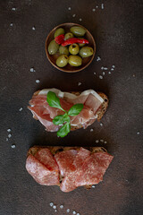 Set of appetizers - crackers with cheese, salami, prosciutto, tomato, olives and salad on dark brown background 