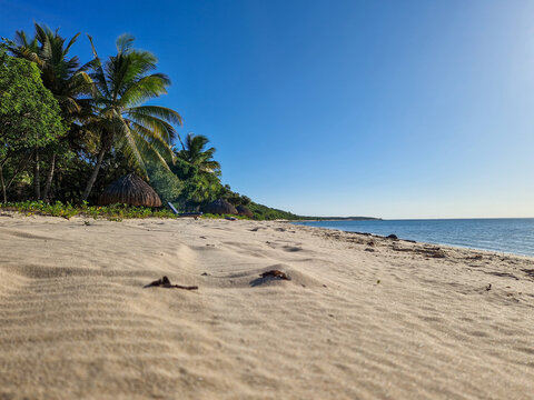 Ein wei&szlig;er Sandstrand mit Palmen, blauem Meer und klarem Himmel bei untergehender Sonne in Mosambik, Afrika 
