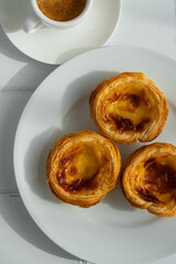 Three pastel de nada on white plate and espresso coffee on white tiled surface.