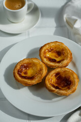 Three pastel de nada on white plate and espresso coffee on white tiled surface.