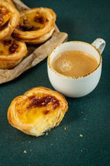 Traditional Portuguese pastel de nata and cup of espresso on green surface.