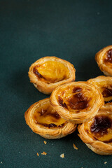 Pile of traditional Portuguese pastel de nata in dawn right corner on green surface.