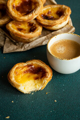 One bitten and three whole traditional Portuguese pastel de nata and cup of espresso on green surface.
