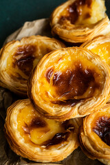 Pile of fresh traditional Portuguese pastel de nata on paper bag on green surface.