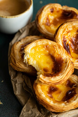 Pile of fresh traditional Portuguese pastel de nata on paper bag and cup of espresso on green surface.