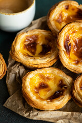 Pile of fresh traditional Portuguese pastel de nata on paper bag and cup of espresso on green surface.