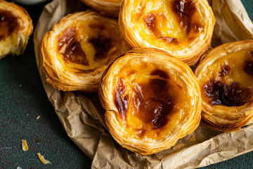 Pile of fresh traditional Portuguese pastel de nata on paper bag on green surface.