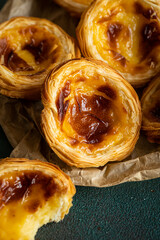 Pile of fresh traditional Portuguese pastel de nata on paper bag on green surface.
