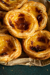 Pile of fresh traditional Portuguese pastel de nata on paper bag on green surface.