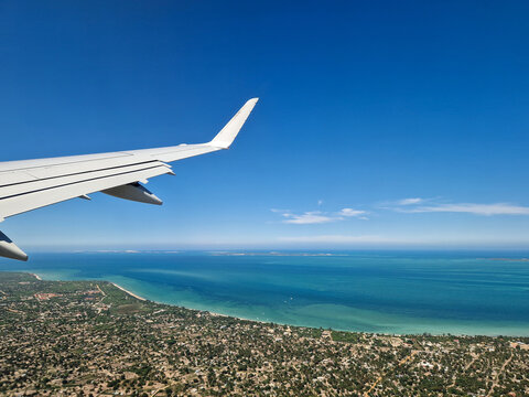 Eine Embraer E190 startet vom Flughafen Vilankulos in Mosambik, Afrika, im Vordergrund die Tragfl&auml;che und im Hintergrund die K&uuml;ste mit Strand und dem blauen Meer