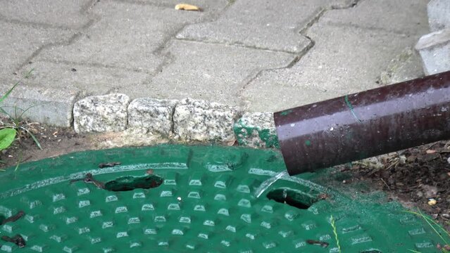 Regenwasser l&auml;uft aus einer Regenrinne in ein Gullideckel