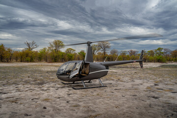 Ein grauer Robinson R44 Hubschrauber bereit zum Abflug zu einer Flugsafari bzw. einem Rundflug über die Savanne des Okavango Delta in Botswana, Afrika - obrazy, fototapety, plakaty
