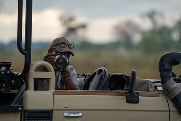 Ein Safari Guide sitzt auf dem Fahrersitz seines Safari Jeeps und fotografiert mit seiner Kamera die Wildtiere in Botswana, Afrika - obrazy, fototapety, plakaty