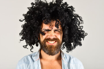 Fototapeta na wymiar Bearded man in black wig. Angry man with beard and mustache in curly wig. Bearded hipster in black curly afro wig. Male in periwig. Party time. Barbershop advertising. Stylish guy with black hair.