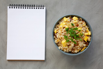 Homemade Fried Rice with Bacon and Egg in a Bowl, blank notepad, top view. Flat lay, overhead, from above. Copy space.