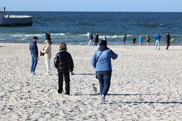 Człowiek z psem na smyczy spaceruje po plaży nad morzem.  - obrazy, fototapety, plakaty