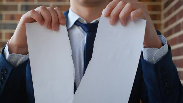 Irritated man tears up a paper contract, contract or application for the calculation of an employee, close-up