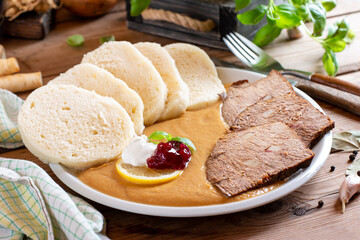 Dumpling with sirloin sauce (traditional Czech food "svickova") with cranberry and beef fillet on plate on the table.