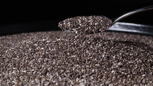 Slow motion of beautiful natural dried chia seeds falling down from a teaspoon. Close-up of organic black and white Salvia Hispanica seeds. Concept of healthy lifestyle, vegetarian or vegan food diet.