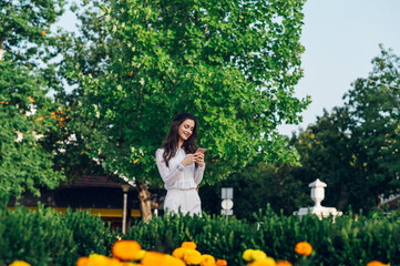 A chic young woman is standing in a city park and smiling at her phone while browsing the internet...