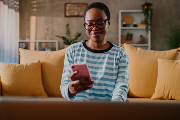 African american woman using laptop and a smartphone while sitting on a sofa at home