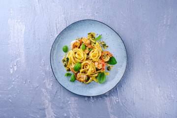Traditional Italian tagliatelle ai gamberoni pasta with king prawns and herbs served as top view on a design plate with copy space