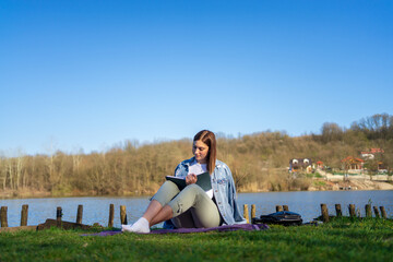 Fototapeta premium Woman at lakeside writing in a notebook. Nature concept. Self reflection.