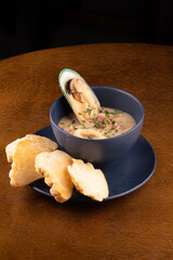 bowl of seafood chowder with toasted New Zealand mussels and green onions on wooden table