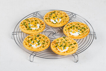 Round corn waffles with soft cottage cheese and greens, on a metal serving stand. White background