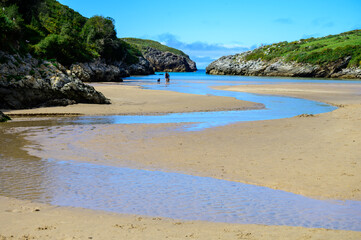 View on Playa de Poo during low tide near Llanes, Green coast of Asturias, North Spain with sandy beaches, cliffs, hidden caves, green fields and mountains.