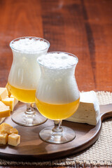 Glasses of Belgian light blonde beer made in abbey and wooden board with variety of belgian cheeses