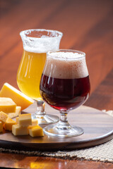 Glasses of Belgian yellow blond and dark brown beer made in abbey and wooden board with variety of belgian cheeses