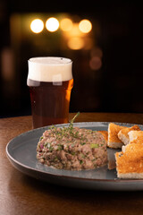 portion of raw beef tartar with spices on blurred background with pint of ale beer on blurred background