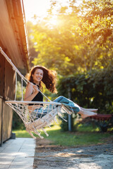 happy young female riding on macrame swing chair near country house outdoors - obrazy, fototapety, plakaty
