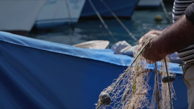 Fisherman is Repairing Fishnets on Fishing Boat in Dock